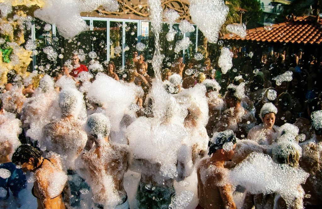 Young people partying in an open air club. Spring break student party with foam.